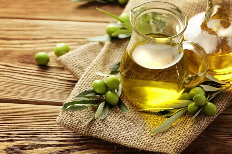 A glass jug of olive oil with fresh olives on burlap
