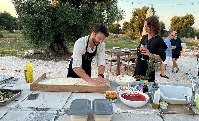 A chef stretching pizza dough at an outdoor table in the olive grove
