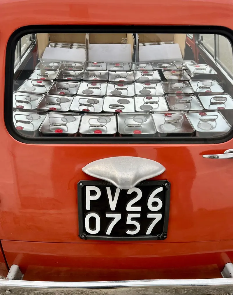 Crates of olive oil tins in the back of a red Fiat